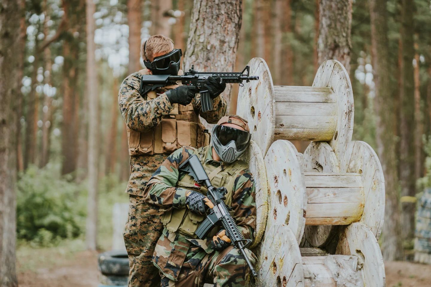 Divi airsofta spēlētāji, viens ir paslēpies, otrs tēmē uz pretinieku.