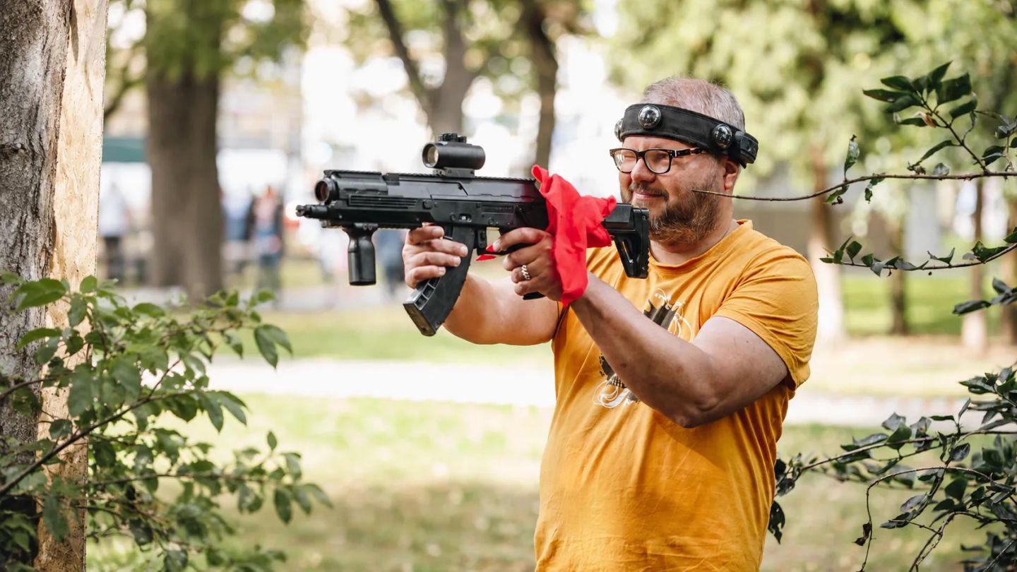 A laser tag game on a sunny day, with a man wearing an orange T-shirt.