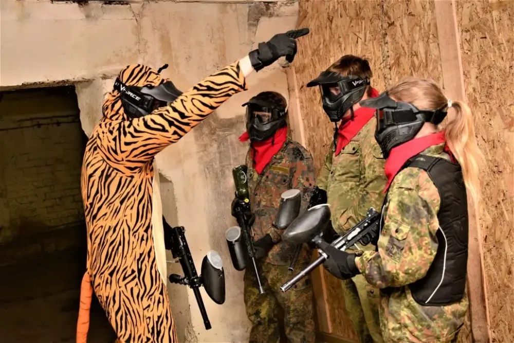 TĪĢERA KOSTĪMĀ INSTRUKTORS STĀSTA PEINTBOLA INSTRUKTĀŽU SPĒLĒTĀJIEM
