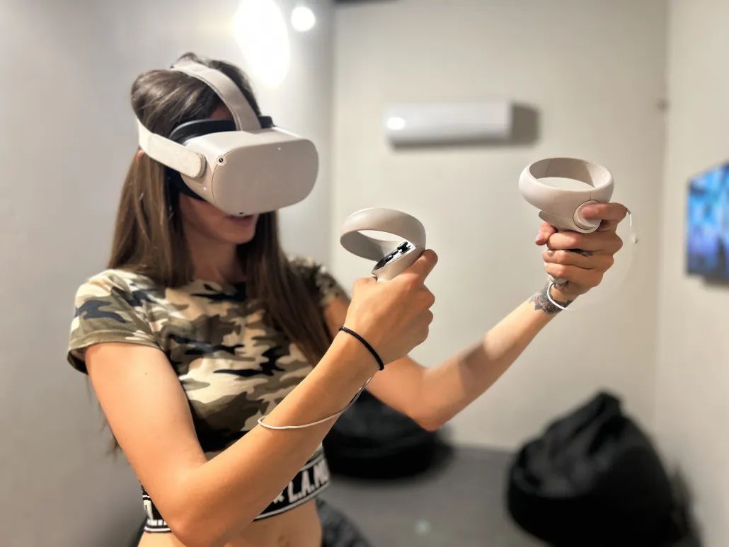 Girl wearing a VR headset and playing virtual reality games, enjoying an immersive gaming experience at GUNSnLASERS entertainment park in Riga.