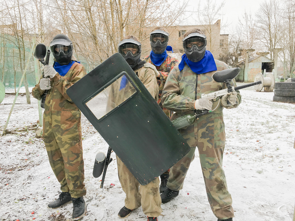 Klases ekskursijā zilā komanda ar peintbola un lāzertag ieročiem rokās pozē pie bāzes.